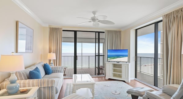 A hotel room with a balcony, a TV, a sofa, a coffee table, and a lamp. - White Caps 1006 by Liquid Life (Orange Beach)