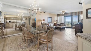 A spacious living area with a glass dining table, wicker chairs, a chandelier, and a view to the outside. - Romar House 304A by Liquid Life (Orange Beach)