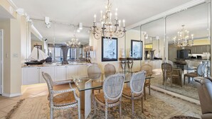 A dining area with a glass table, wicker chairs, a chandelier, and a large mirror reflecting the kitchen. - Romar House 304A by Liquid Life (Orange Beach)