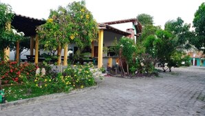 Un patio con piso de baldosas, una zona de estar techada y diversas plantas y flores.