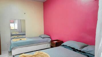 A room with two beds, a mirror, and a red wall.