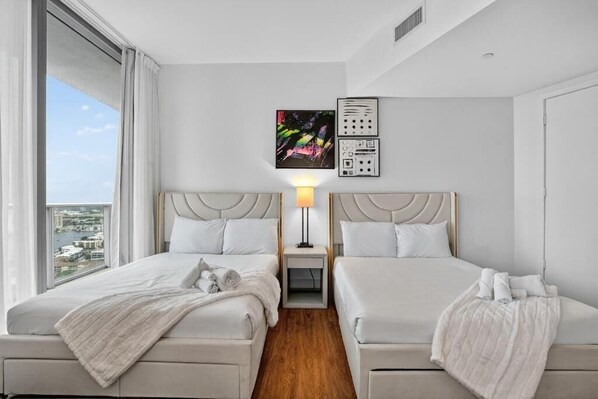 A hotel room with two beds, a nightstand, a lamp, and artwork on the wall. - Lyfe Resort Hollywood Florida (Hollywood)