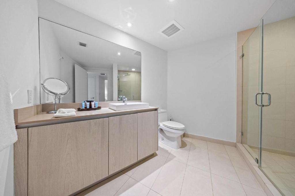 A modern bathroom with a large mirror, a sink, a toilet, and a glass shower enclosure.