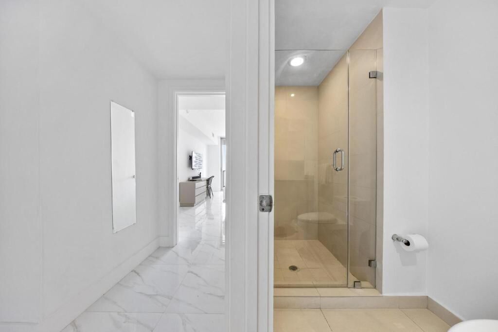 Un baño moderno con cabina de ducha de vidrio, un inodoro y un dispensador de papel higiénico blanco.