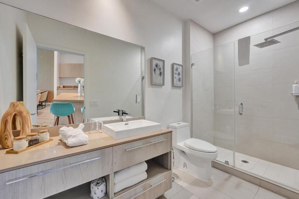 Een moderne badkamer met een grote spiegel, een witte wastafel, een toilet en een douchecabine met glazen wanden.