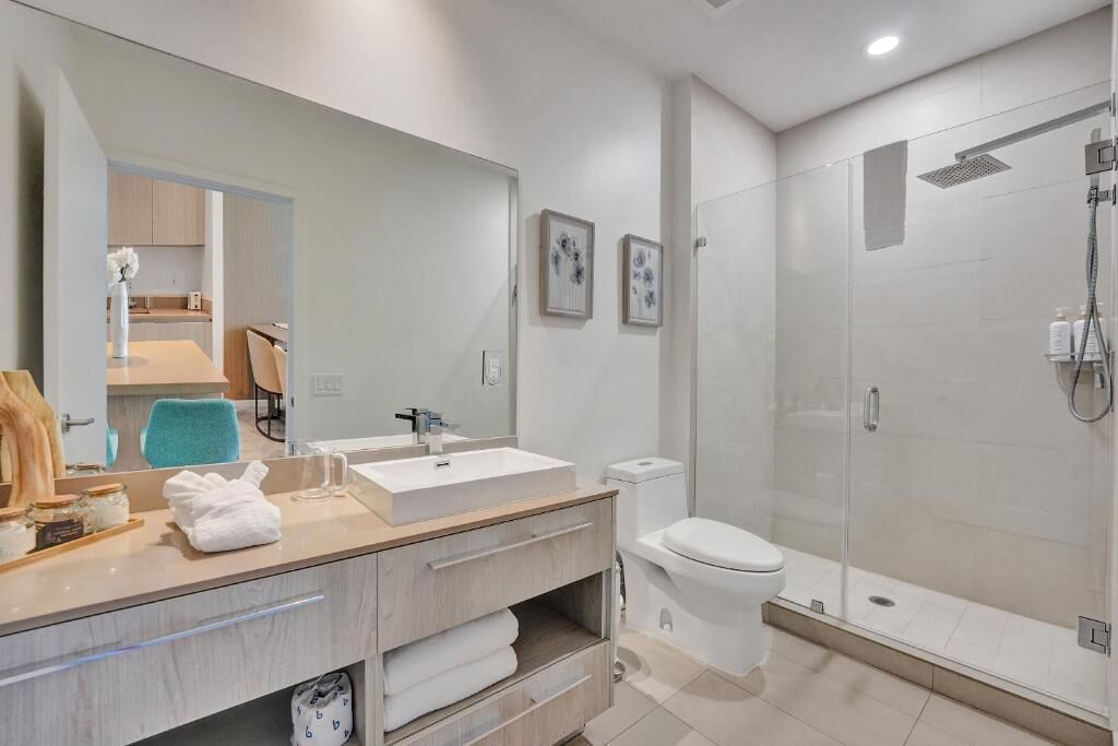 A modern bathroom with a large mirror, a sink, a toilet, and a glass-enclosed shower.