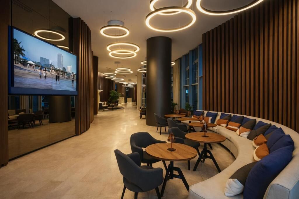 Un vestíbul modern amb una zona d'estar corba, una pantalla de televisió gran i llums de sostre circulars.