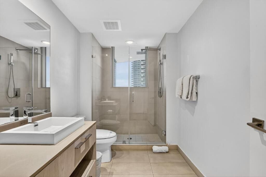 A modern bathroom with a glass-enclosed shower, a large mirror, and a white toilet.