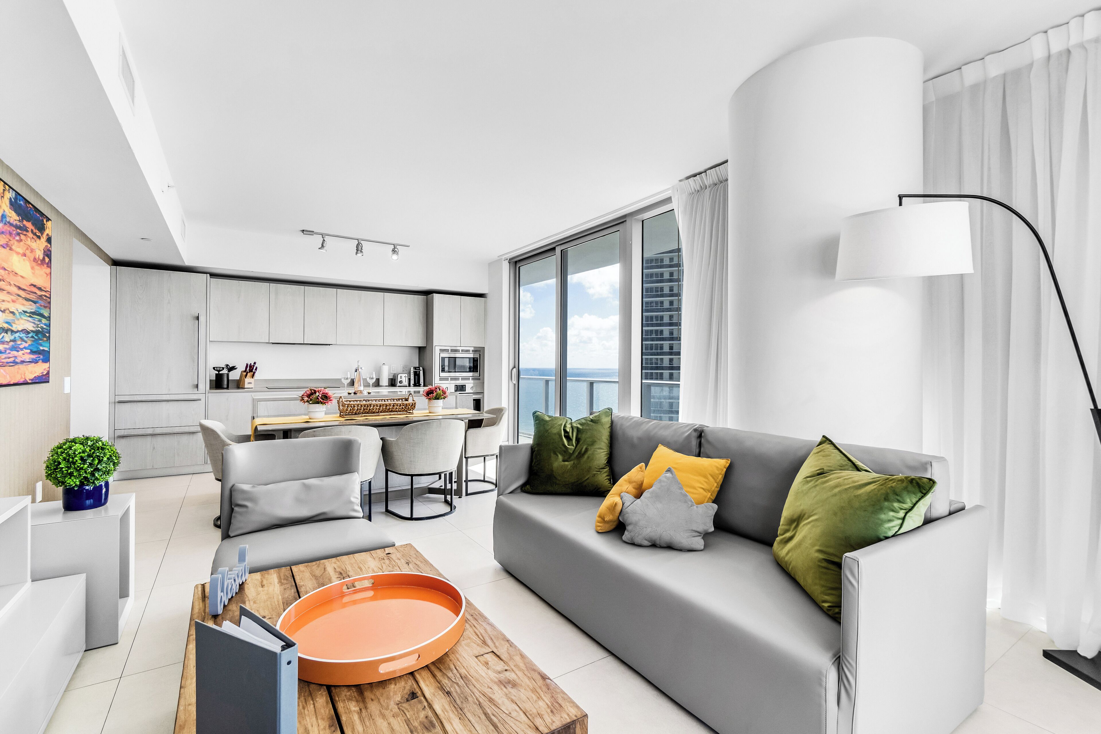 A modern living room with a grey sofa, a coffee table, and a view of the city through large windows.