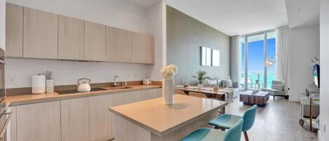 A modern kitchen with a central island, bar stools, and a view of the living area with a large window.