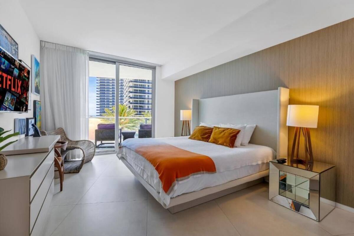 A modern hotel room with a large bed, a desk, a chair, and a balcony with a city view.