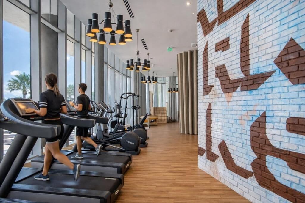 A gym with treadmills, elliptical machines, and a brick wall with a geometric pattern.