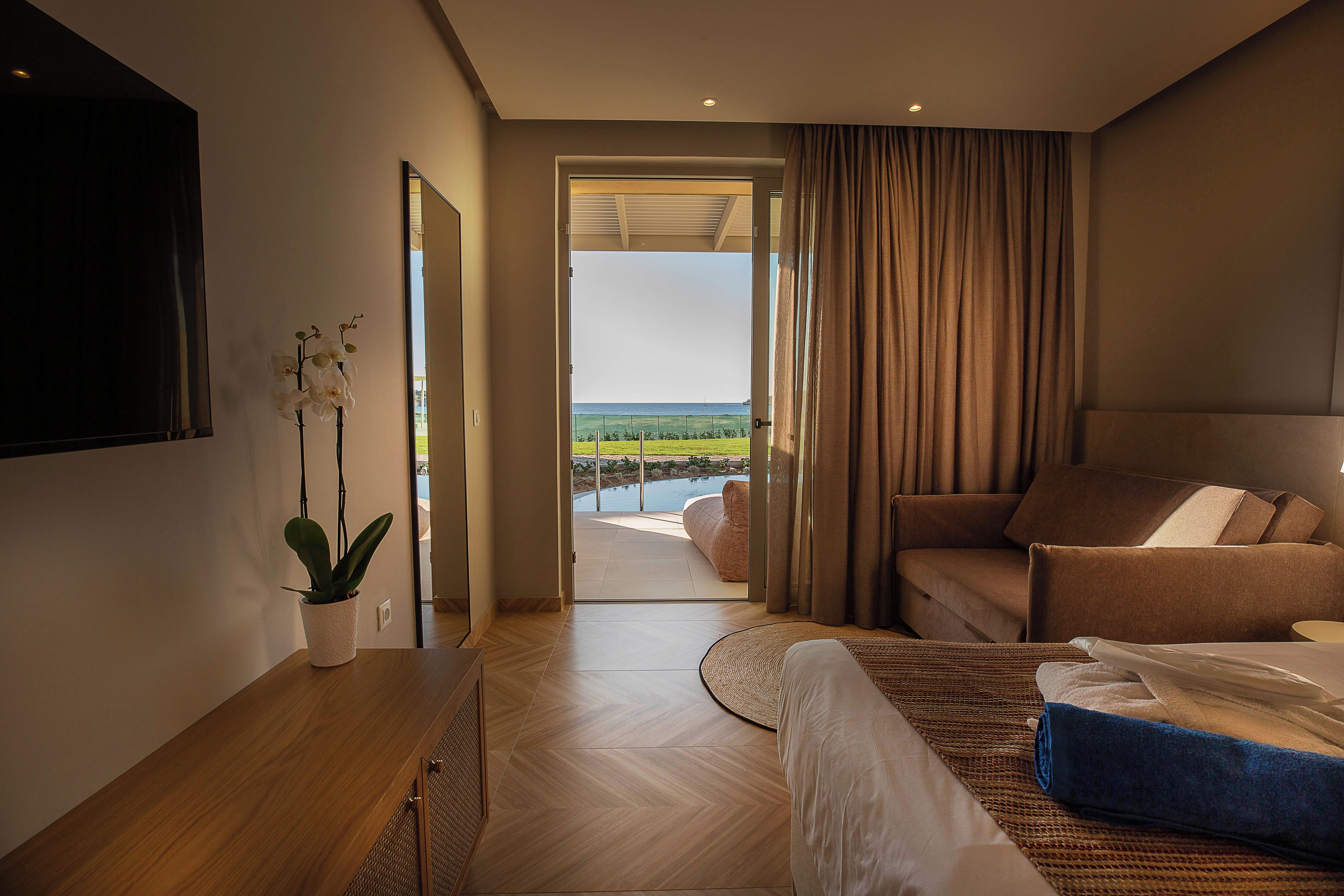 Een moderne hotelkamer met een bed, een zithoek, een potplant en uitzicht op het omliggende landschap.