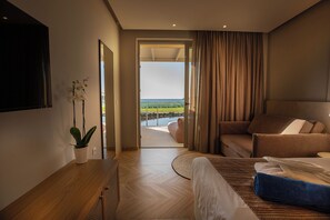 A modern hotel room with a bed, a seating area, a potted plant, and a view of the outdoors. - Maxion Hotel (Rhodes)