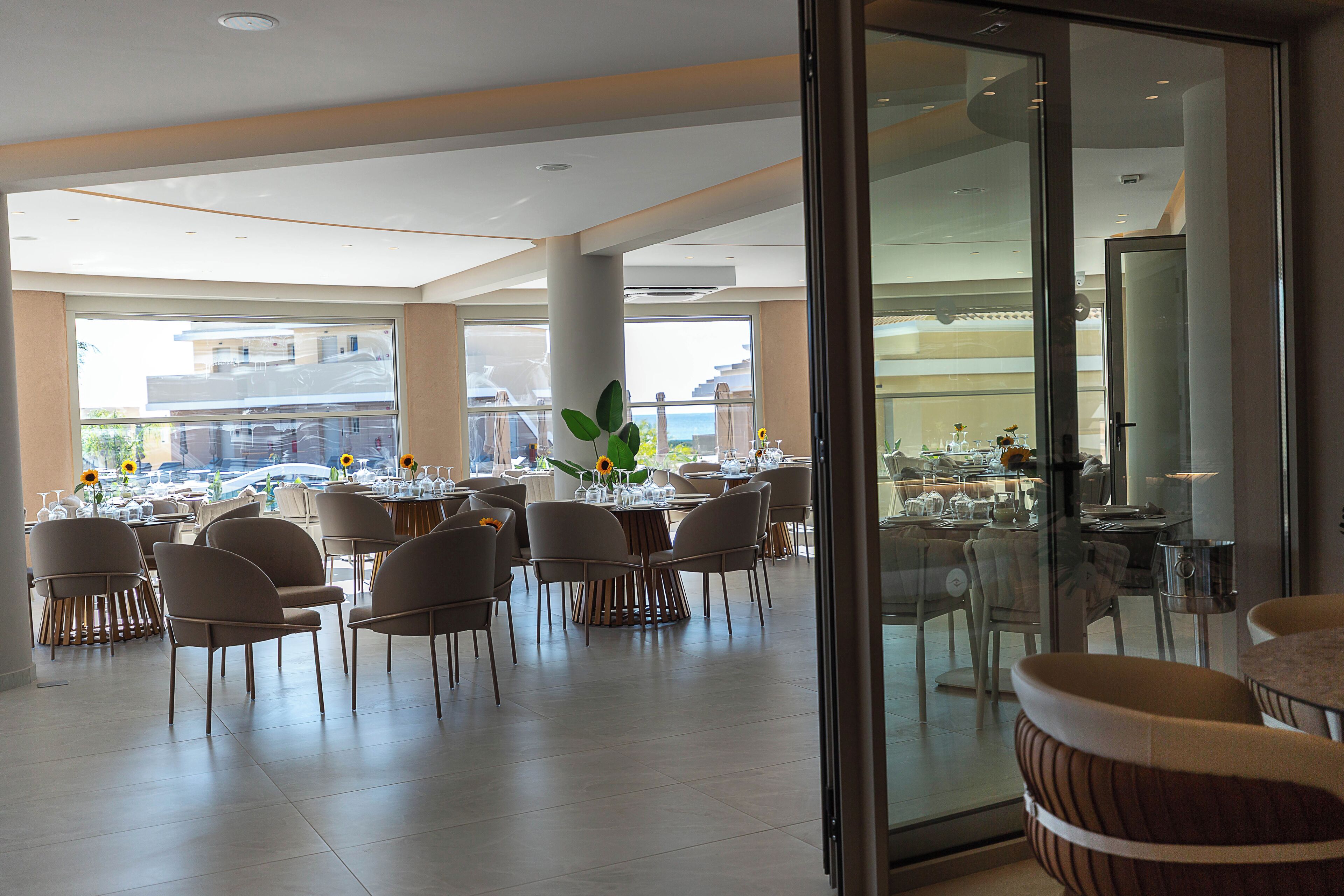 Un comedor amplio con varias mesas y sillas, ventanas grandes y vistas al exterior.
