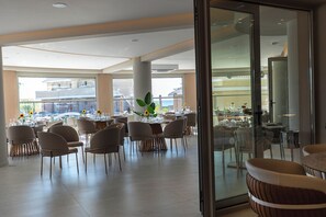 A spacious dining area with multiple tables and chairs, large windows, and a view of the outside. - Maxion Hotel (Rhodes)
