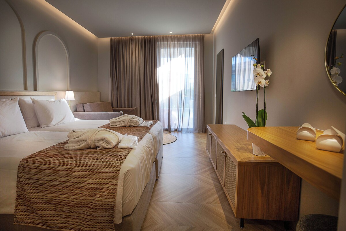 Una habitación de hotel con cama, escritorio, silla, televisor y ventana con cortinas.