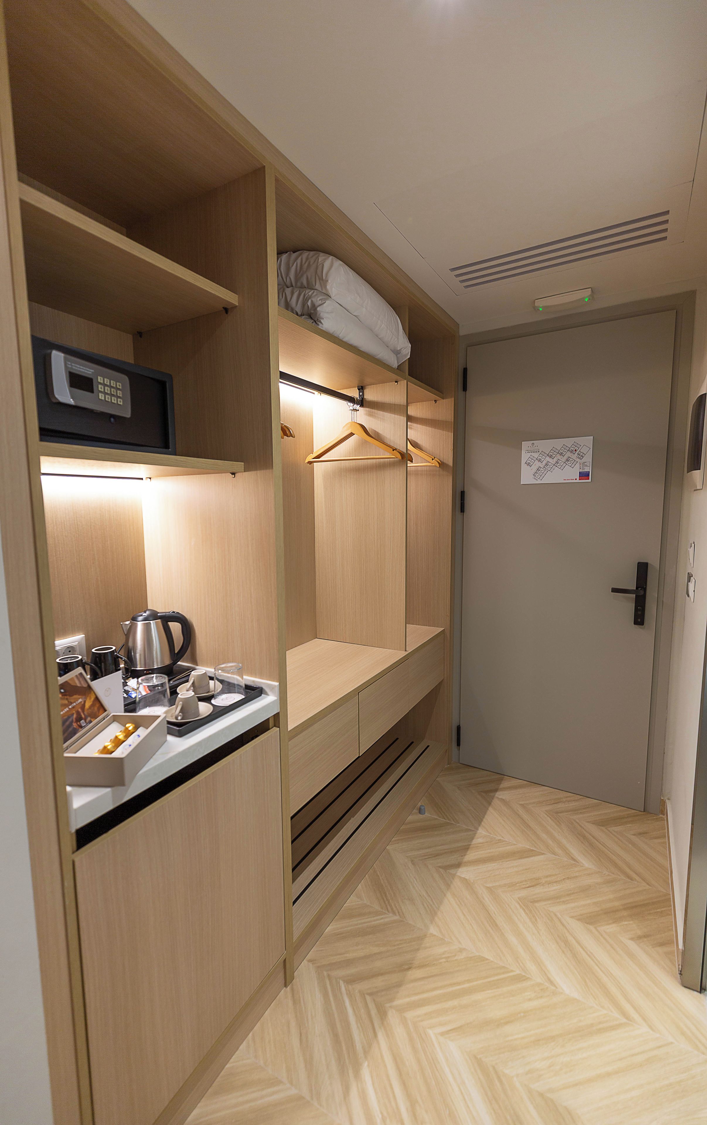 Habitación de hotel compacta con kitchenette, una cama con almohada, perchero y puerta con un letrero.