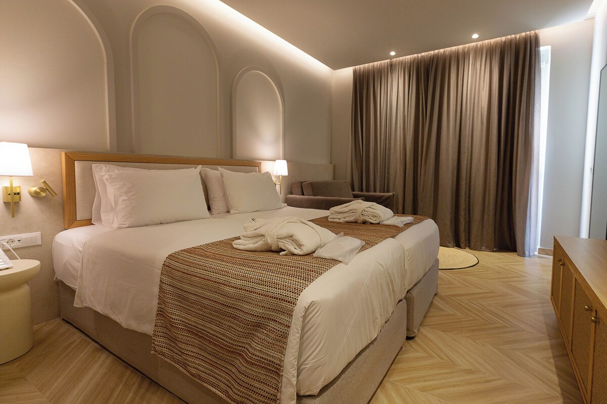 A hotel room with a large bed, two bedside tables, a desk, and a window with curtains.