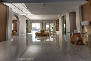 A spacious lobby with a reflective floor, a central seating area, and a view of the outside through large windows. - Maxion Hotel (Rhodes)