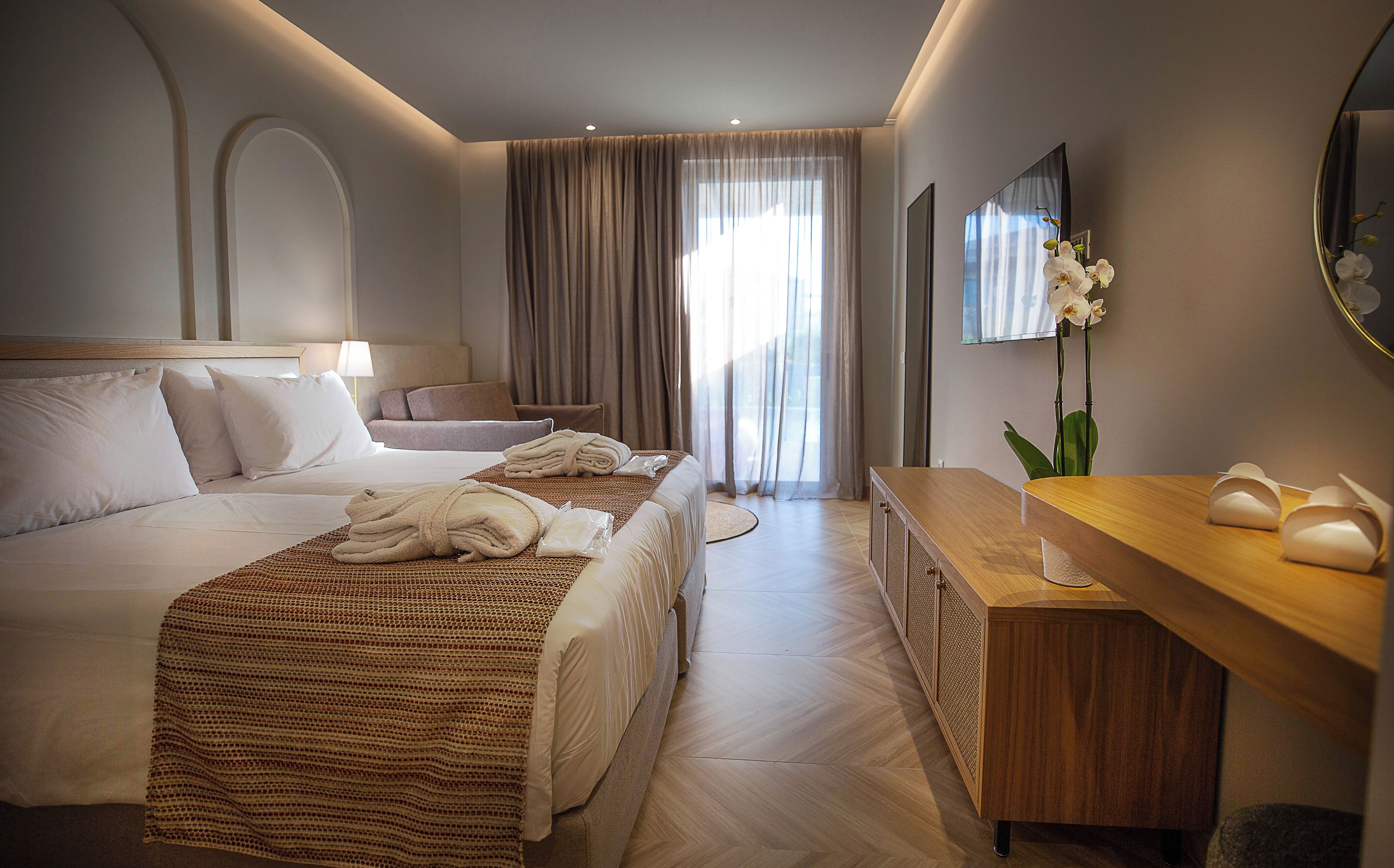 A hotel room with a bed, a desk, a chair, a TV, and a window with curtains.