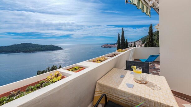 A balcony with a table, chairs, and a view of the sea.