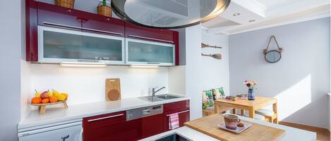 A modern kitchen with red cabinets, a built-in dishwasher, and a wooden dining table with a vase of flowers.