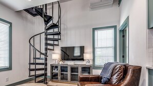 A modern living room with a spiral staircase, a flat-screen TV, leather furniture, and a wooden coffee table. - North Gable- Bunkhouse in Steele Park with Private Pool and Hot Tub access (Carlton Landing)