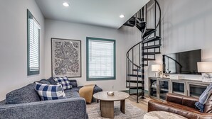 A living room with a sofa, a coffee table, a brown leather couch, a spiral staircase, and a flat-screen TV. - North Gable- Bunkhouse in Steele Park with Private Pool and Hot Tub access (Carlton Landing)