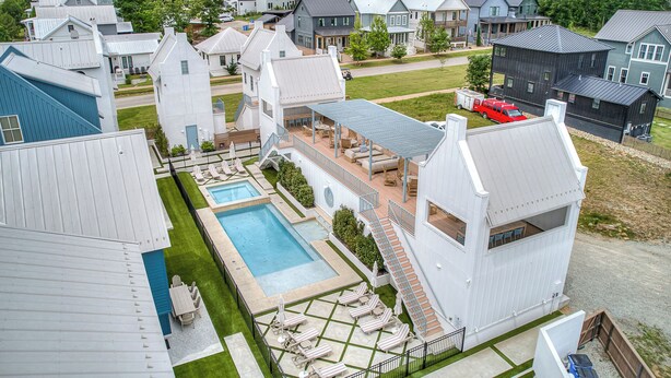 A residential area with modern houses, a swimming pool, and a patio with lounge chairs. - North Gable- Bunkhouse in Steele Park with Private Pool and Hot Tub access (Carlton Landing)