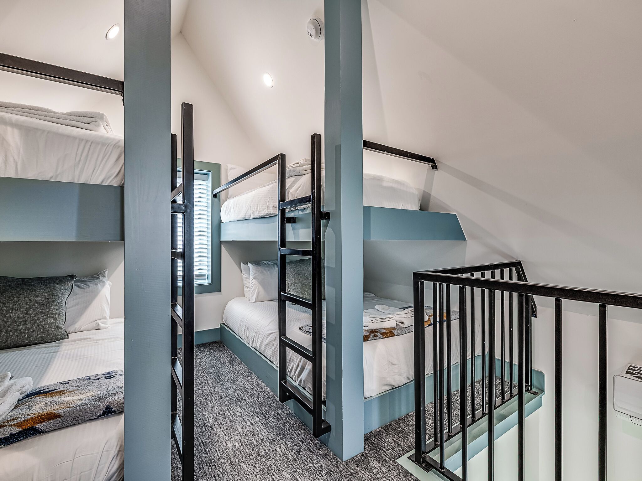 A bunk bed room with a window, a staircase, and a ceiling light.