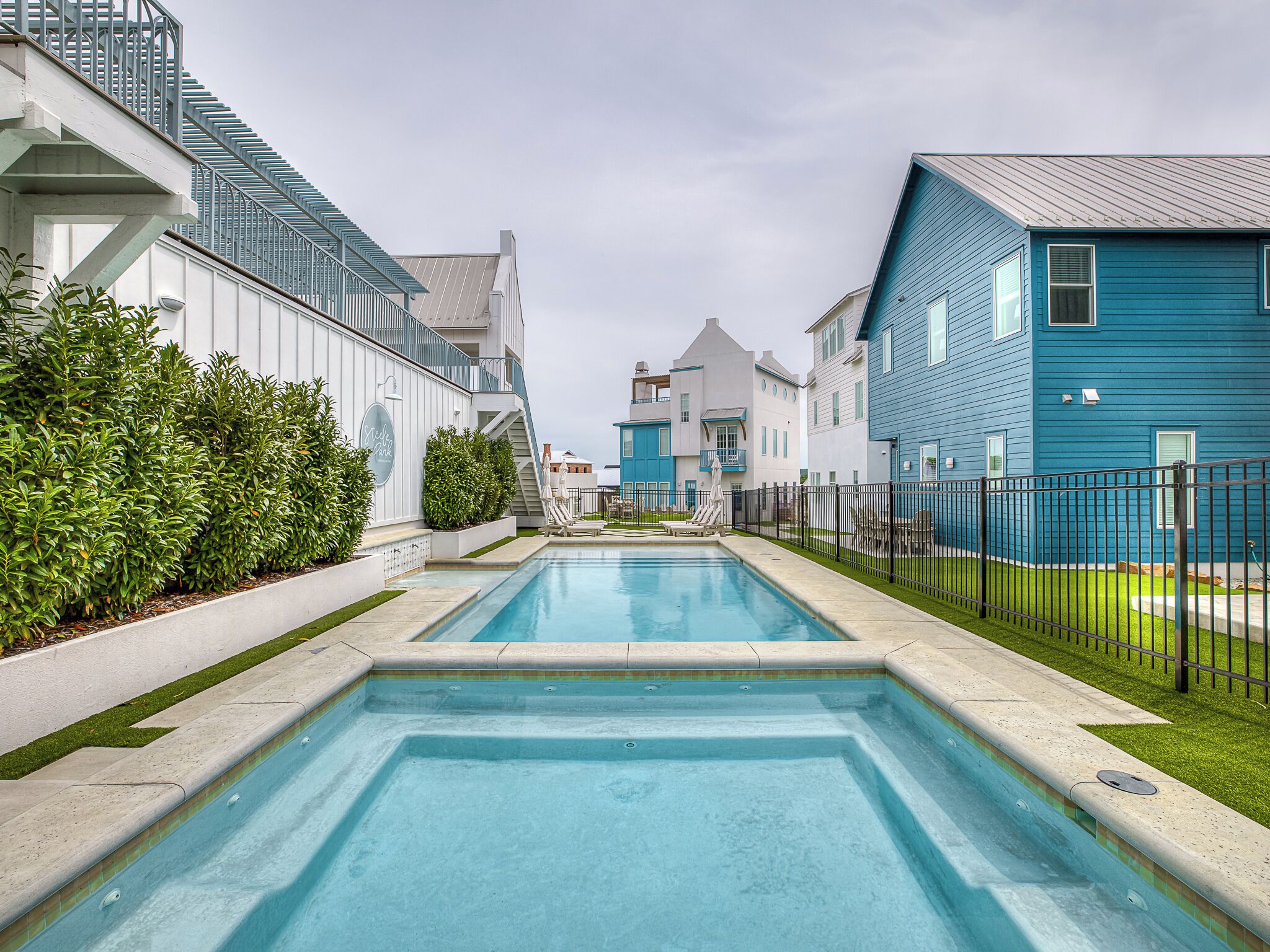 Une piscine avec vue sur des bâtiments modernes, un espace clos et une pelouse bien entretenue.