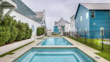 A swimming pool with a view of modern buildings, a fenced area, and a well-maintained lawn.