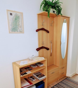 Une armoire en bois avec un miroir, un porte-manteau et une étagère contenant des livres et un verre.