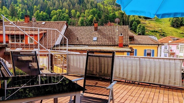 A terrace with a chair, a table, and a blue umbrella.