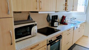 A kitchen with wooden cabinets, a microwave, a coffee maker, a red kettle, and a sink.