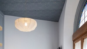 Un dormitorio con cama, lámpara colgante, espejo y ventana con cortinas.