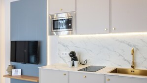 Una cocina moderna con microondas integrado, un lavamanos y un televisor sobre una pared azul.