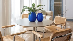 Una habitación con una mesa redonda, cuatro sillas de mimbre, dos jarrones azules y una planta.