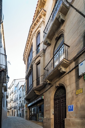 A street with historic buildings, a closed shop, and a blue AT sign. - 4Duques Apartments (Cáceres)