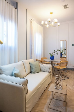 Un salon moderne comprenant un canapé, une table à manger, des chaises, un vase avec des plantes et un lustre.