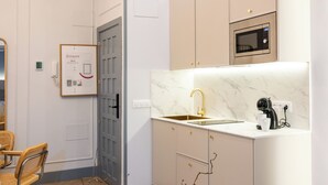 Een moderne keuken met een marmeren aanrechtblad, een ingebouwde magnetron en een klein spoelbakje.