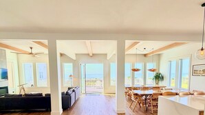 A spacious living area with a wooden floor, a dark sofa, and a dining area with a white island and wooden chairs.
