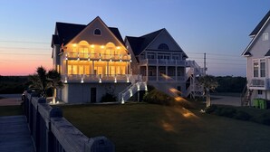 A large, multi-story house with a prominent balcony and a well-lit front porch.