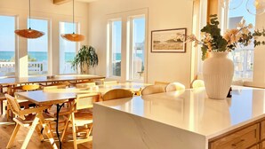 A modern kitchen with a central island, wooden flooring, and large windows overlooking the ocean.