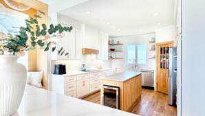 A modern kitchen with white cabinetry, a central island, wooden flooring, and pendant lighting.