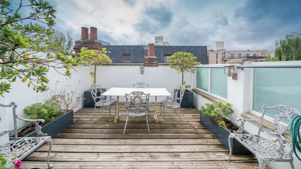 Eine Dachterrasse mit Holzboden, Metallstühlen, einem Tisch und Topfpflanzen.