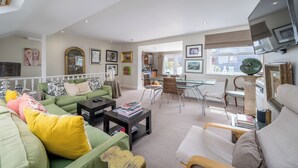 Ein geräumiger Wohnbereich mit einem grünen Sofa, einem Esstisch und einem an der Wand befestigten Fernseher.