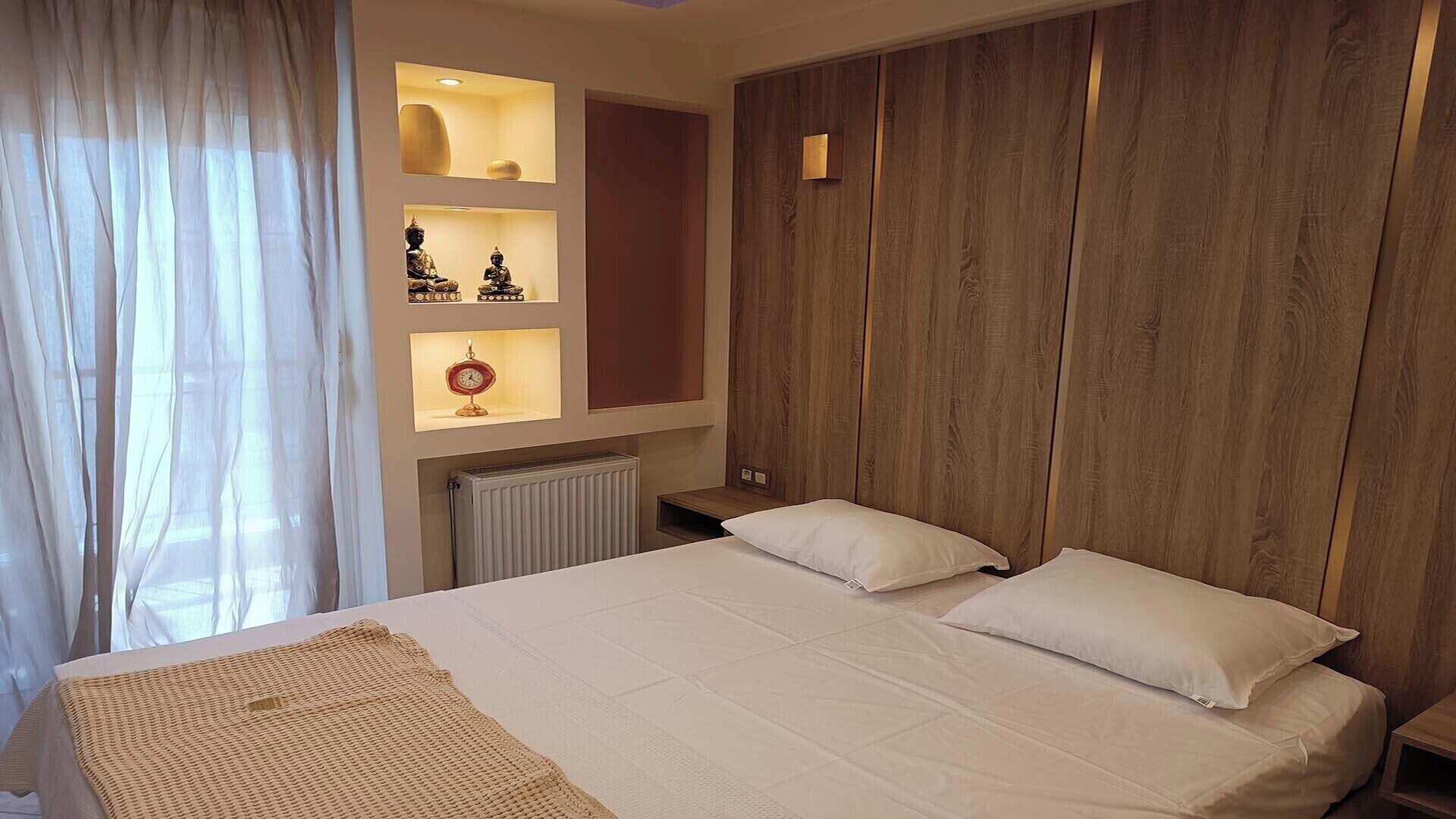 A bedroom with a large bed, wooden panel walls, and a shelf with decorative items.