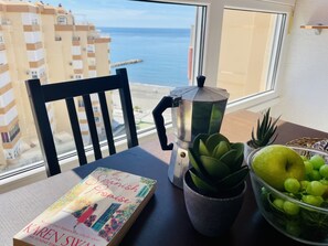 Una mesa con un libro, una cafetera, una planta suculenta y un cuenco de uvas.